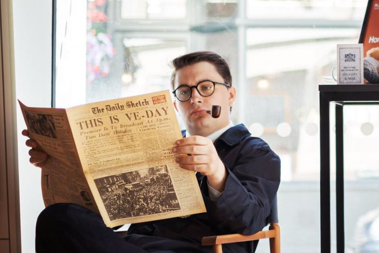 Man smoking a pipe reading a newspaper with the headline "This is VE-Day"