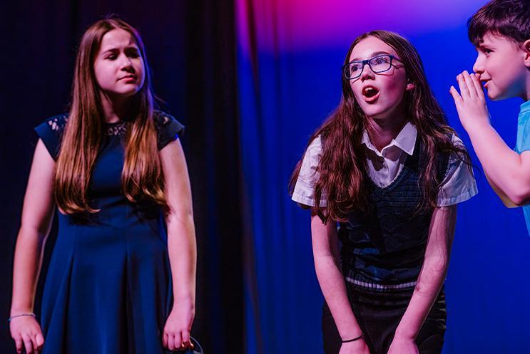 Three young performers - one is whispering into another's ear