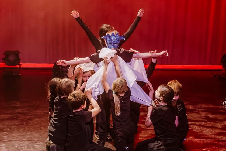 Young performers crouching in a circle around one masked performer