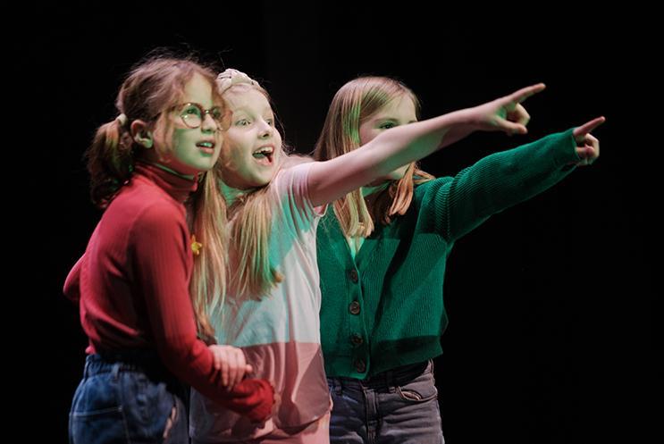 Three children performing on stage and pointing to the audience