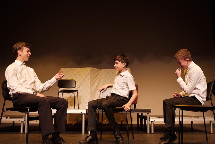 Three young performers on stage sat in chairs