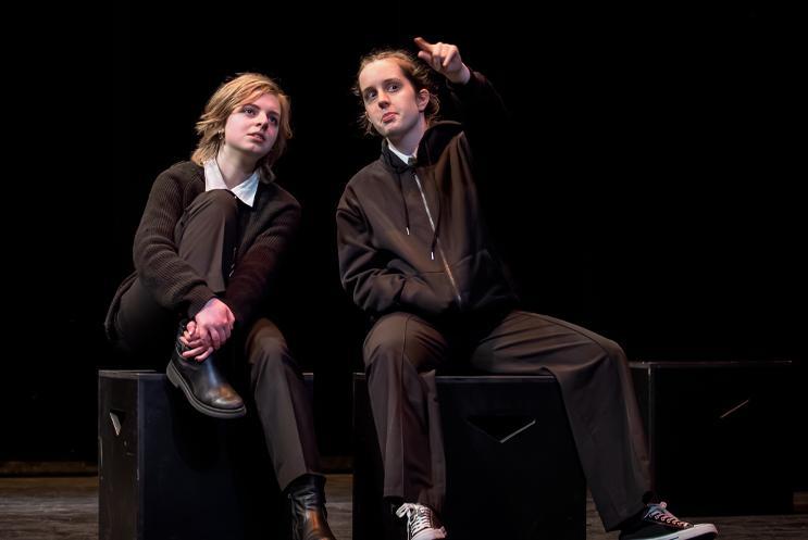 Two young performers in school uniform sat pointing upward.