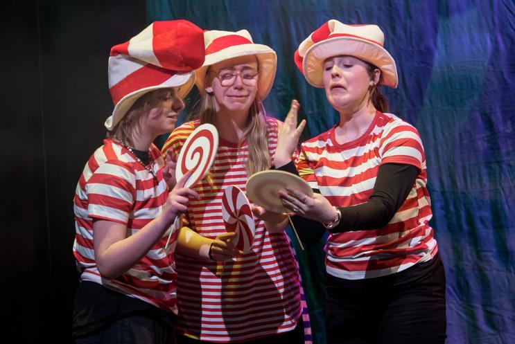 Three young performers dress in stripey red and white clothes, holding lollipops and looking happy.