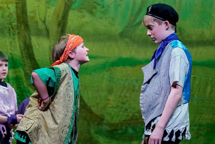 Two young performers stood in front of a green backdrop and arguing.
