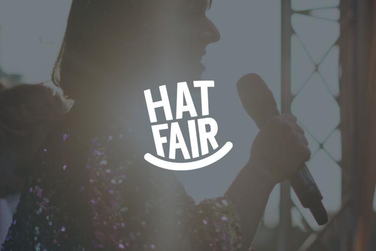 The Hat Fair logo overlaying a background image of a person singing
