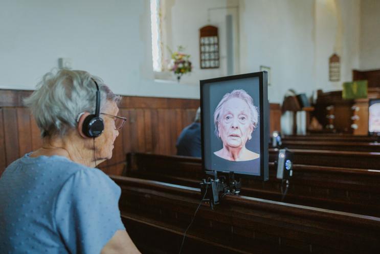Lady wearing headphones watching a portrait screen of a talking head.