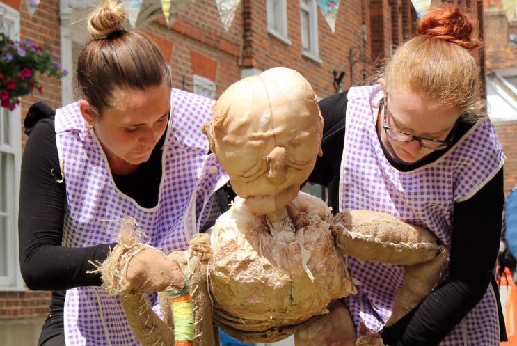 Two puppeteers performing outdoors with a life size puppet to an audience